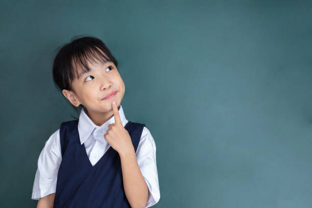 asian chinese little girl thinking with finger on chin - blackboard education classroom photography imagens e fotografias de stock