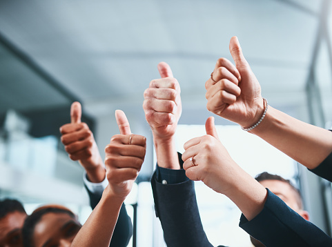 Closeup shot of a group of businesspeople showing thumbs up in an office