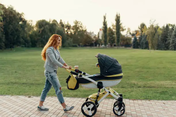 A young mother enjoying the park walk with her little child relaxing in his baby trolley.