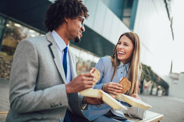 Smiling businessmen with sandwiches sitting in front of the office building - lunch break Smiling businessmen with sandwiches sitting in front of the office building - lunch break lunch break stock pictures, royalty-free photos & images