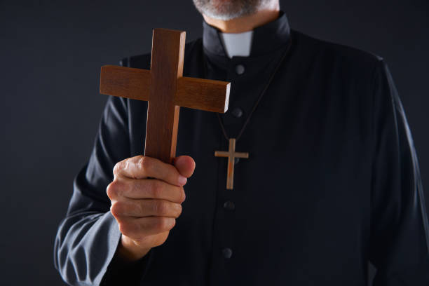 Priest holding cross of wood praying Priest holding cross of wood praying in foreground exorcism stock pictures, royalty-free photos & images