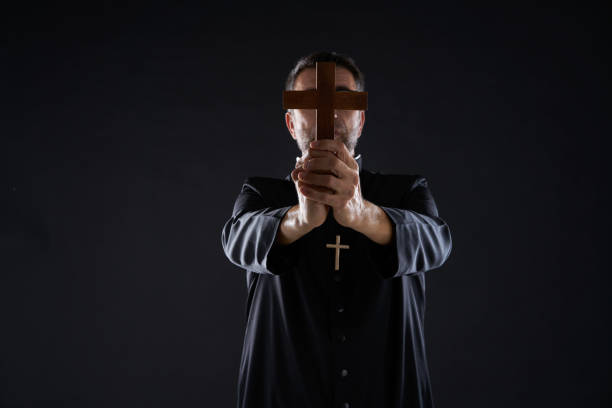 Priest holding cross of wood praying Priest holding cross of wood praying in foreground exorcism stock pictures, royalty-free photos & images