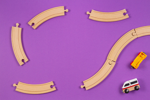 Toy train and wooden rails pieces on purple violet background.
