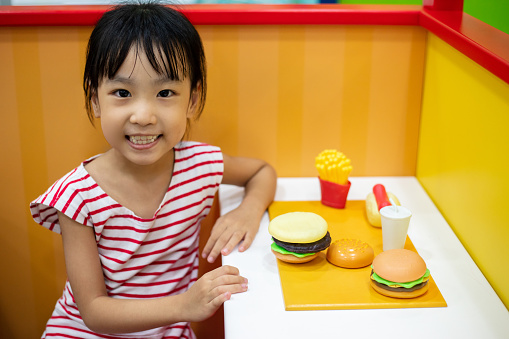 Asian Chinese little girl role-playing at burger store at indoor playground