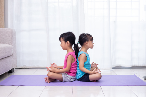 Asian Chinese little sisters practicing yoga pose on a mat in the living room at home