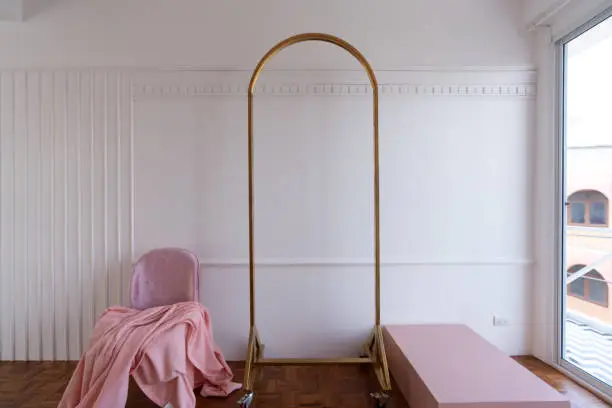 Composition of oldrose blanket setting on mid century modern chair in baby pink color setting in white wooden stripe and classic moulding wall and gold clothes hanger.
