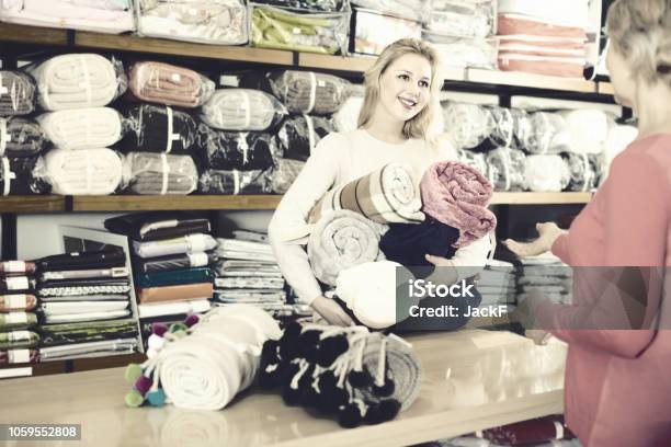 Friendly Female Seller Demonstrating Coverlets To Senior Buyer In Textile Shop Stock Photo - Download Image Now