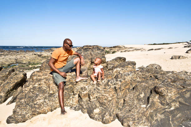 istock Young Man And Child Sitting/Posing By The Seaside. Clear Blue Sky Background 1059568480