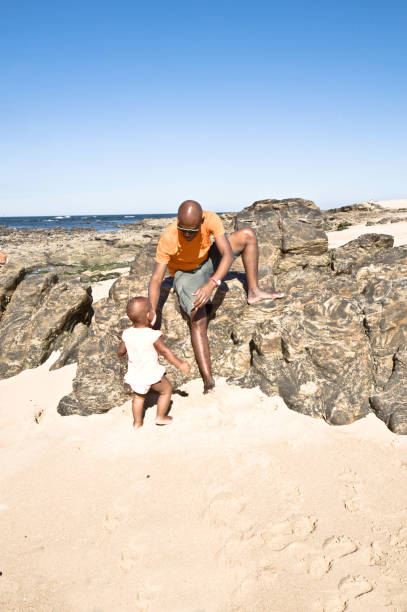 istock Young Man And Child Sitting/Posing By The Seaside. Clear Blue Sky Background 1059569330