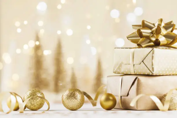 Photo of Christmas gift box against golden bokeh background. Holiday greeting card.