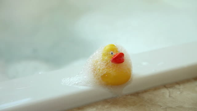 Child grabs rubber ducky from side of tub