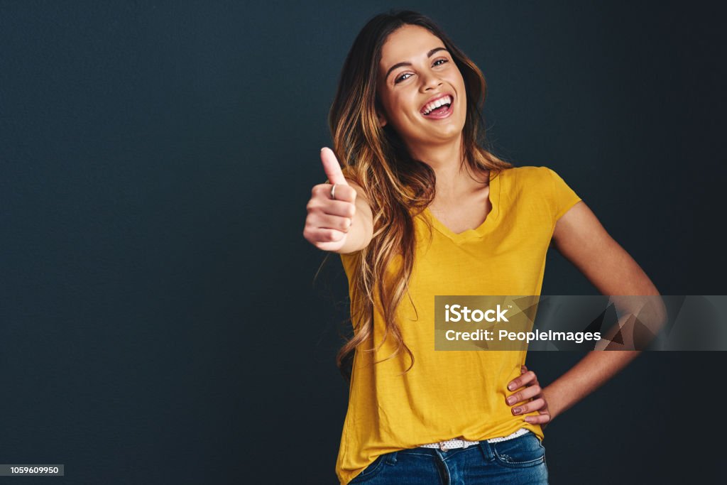 Oh, you know you have my approval Studio shot of an attractive young woman against a dark background Thumbs Up Stock Photo