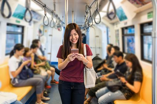 Asian woman passenger with casual suit using the smart mobile phone in the Skytrain rails or subway for travel in the big city, lifestyle and transportation concept