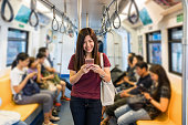 Asian woman passenger with casual suit using the smart mobile phone in the Skytrain rails or subway for travel in the big city, lifestyle and transportation concept