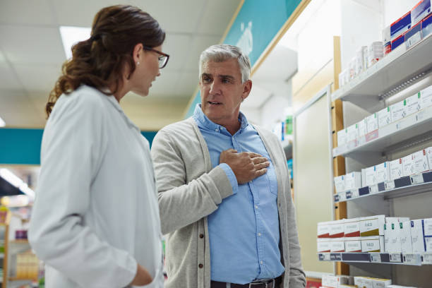 I feel the pain in my chest Shot of a young pharmacist helping a customer in a chemist heartburn photos stock pictures, royalty-free photos & images