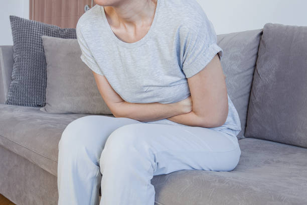 胃の痛み、女性問題。自宅のベッドに座って腹部の痛み。 - 月経前症候群 ストックフォトと画像