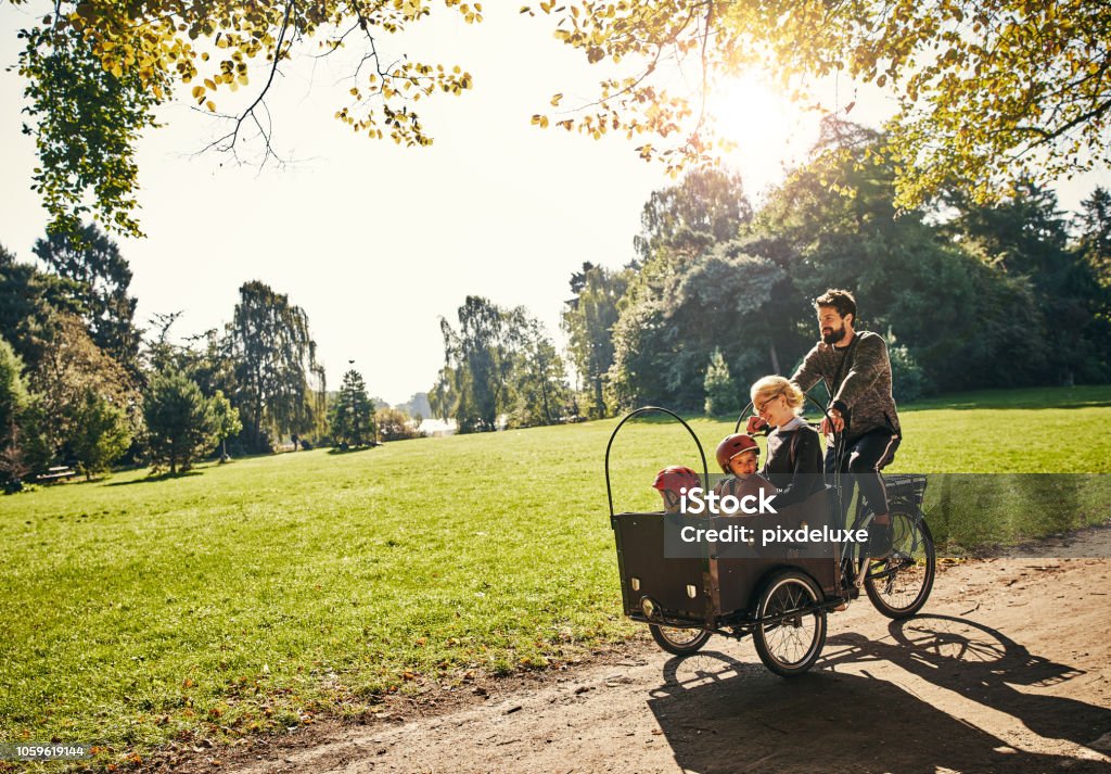 Cycling through the park Full length shot of a young man taking his family around the park on a cargo bike Family Stock Photo