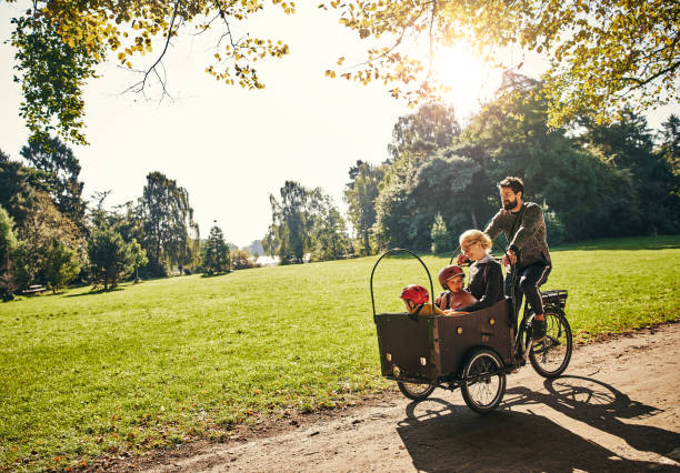 Cycling through the park Full length shot of a young man taking his family around the park on a cargo bike cargo bike photos stock pictures, royalty-free photos & images