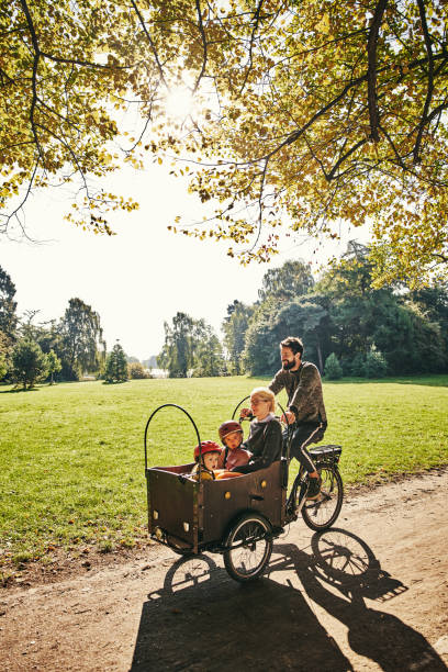 Taking his family around the park Full length shot of a young man taking his family around the park on a cargo bike cargo bike photos stock pictures, royalty-free photos & images