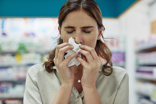 Shot of a young woman sneezing in a pharmacy