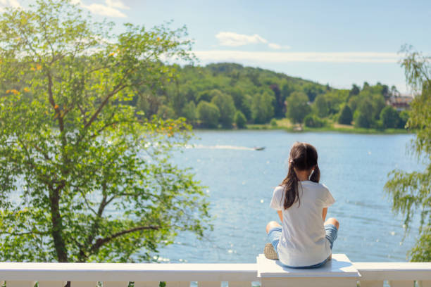 Summer holiday A girl sits on a railing by a lake on a summer day. lake malaren photos stock pictures, royalty-free photos & images