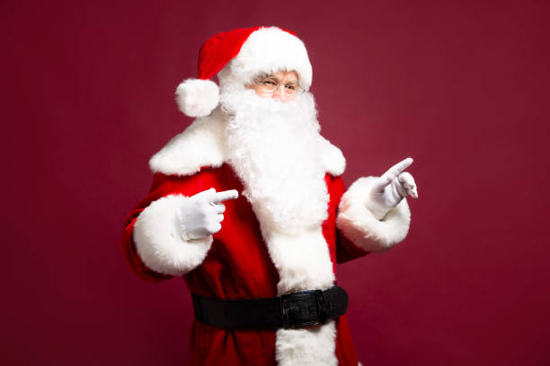 istock Santa Clause pointing by fingers aside while posing on red background 1059636226