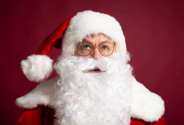 istock Santa Clause in eyeglasses looking up on red background 1059636344