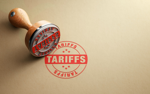Wooden tariffs stamp is sitting on recycled paper background. Horizontal composition with selective focus and copy space.