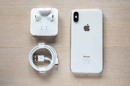 Celje, Slovenia - October 06, 2018: Unpacking the new iPhone. Overhead shot of an rear view of iPhone XS smartphone (with 5.8 inch Retina display, double camera, silver color version with 256 GB memory), lightning to USB cable and EarPods.