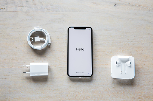 Celje, Slovenia - October 06, 2018: Unpacking the new iPhone. Overhead shot of an iPhone XS smartphone (with 5.8 inch Retina display, welcome screen, silver color version with 256 GB memory), lightning to USB cable, power adapter and EarPods.