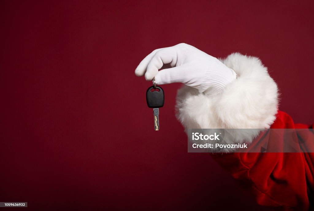 Male hand in white glove and Santa Clause costume holding key on red background, Christmas and New year concept Car Stock Photo