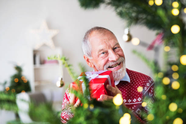 istock A senior man with a present in a wrapped box standing by Christmas tree. 1059637234