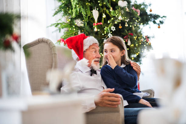 una niña que dice un secreto a su abuelo con sombrero de santa en navidad. - whispering grandparent child grandfather fotografías e imágenes de stock