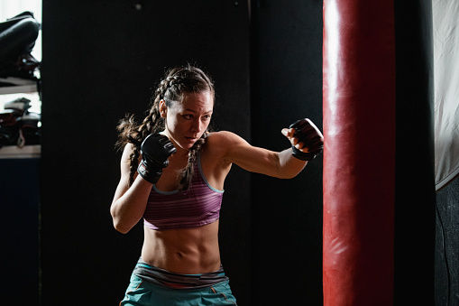 Female boxer is training with a punching bag in the gym.