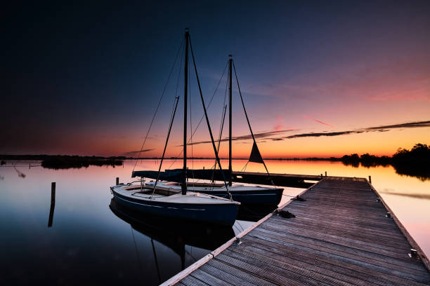 Some small sailboats at a wooden jetty half an hour before dawn in Lake Leekstermeer, The Netherlands