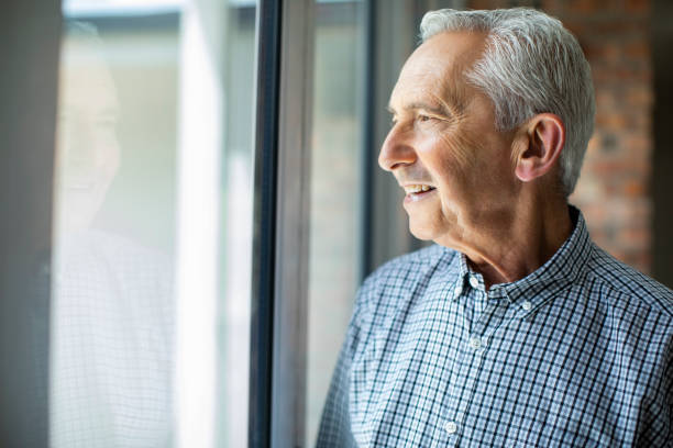 istock Smiling senior man looking through window at home 1059640828