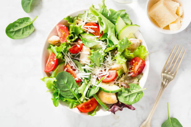 Tasty fresh salad with chicken and vegetables Tasty appetizing fresh salad with chicken, tomatoes, cucumbers and cheese parmesan in bowl on white marble backhground. View from above. Horizontal with copy space. Romaine stock pictures, royalty-free photos & images