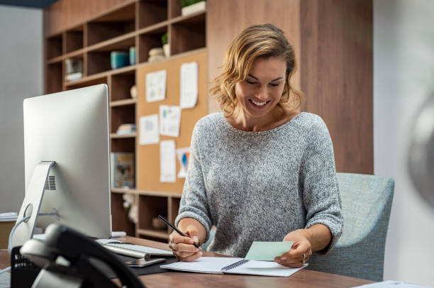 Happy business woman making notes Smiling busy employee in casual reading notes and writing on notebook. Happy mature business woman reading letter and smiling at office. Creative businesswoman writing in book with pencil while taking notes for meeting. 30s 40s activity adult stock pictures, royalty-free photos & images