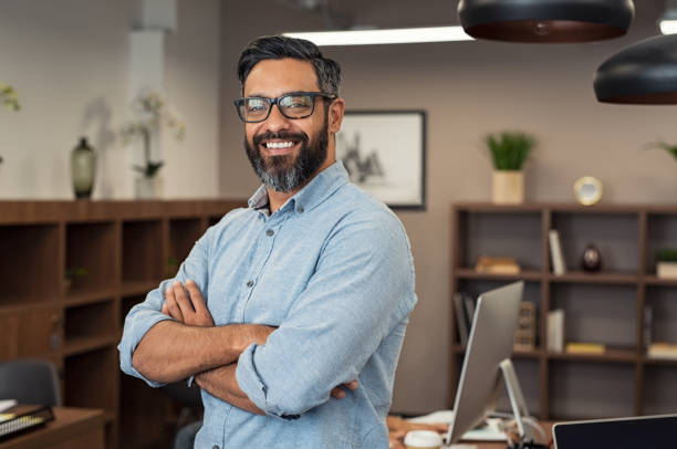 Mature mixed race business man Portrait of happy mature businessman wearing spectacles and looking at camera. Multiethnic satisfied man with beard and eyeglasses feeling confident at office. Successful middle eastern business man smiling in a creative office. mid adult men stock pictures, royalty-free photos & images