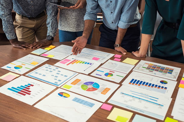 Business casual team working on graphs Financial and business documents on table with multiethnic hands working on it. Latin business manager with colleagues working on new startup project. Closeup business man and businesswoman hands understanding pie and bar graphs during meeting. annual report stock pictures, royalty-free photos & images