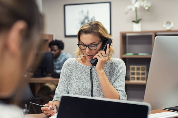 businesswoman talking on phone at office - receptionist customer service customer service representative imagens e fotografias de stock