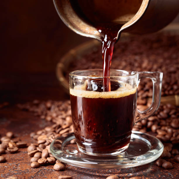 istock Black coffee is poured into a small glass cup from a old copper coffee maker. 1059674782