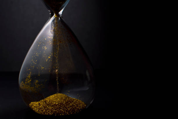 Sand and golden glitter passing through the glass bulbs of an hourglass measuring the passing time as it counts down to a deadline or closure on a black background with copy space stock photo