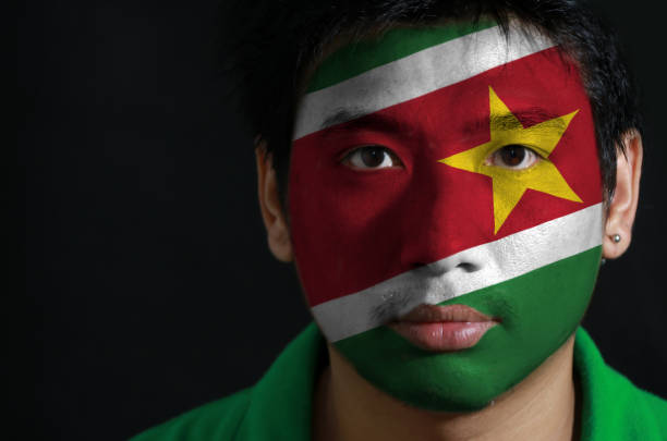 Portrait of a man with the flag of the Suriname painted on his face on black background. stock photo