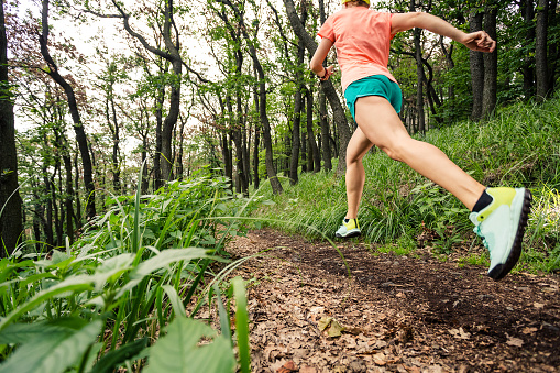 Young woman running in green forest. Endurance sport training. Female trail runner cross country running. Sport and fitness concept outdoors in nature.