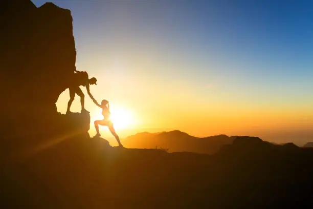 Teamwork couple helping hand trust help silhouette in mountains, sunset. Team of climbers man and woman hikers, help each other on top of mountain, climbing together, inspiring landscape on Gran Canaria.