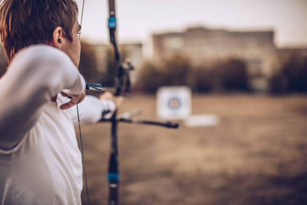 Man aiming at target One man, young archer with bow and arrow training alone outdoors. bulls eye stock pictures, royalty-free photos & images