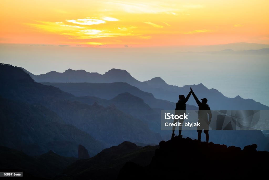 Teamwork couple climbing helping hand Teamwork couple helping hand trust help, silhouette success in mountains. Team of climbers man and woman. Hikers celebrate with hands up, help each other on top of mountain, climbing together, beautiful sunset landscape. Aspirations Stock Photo