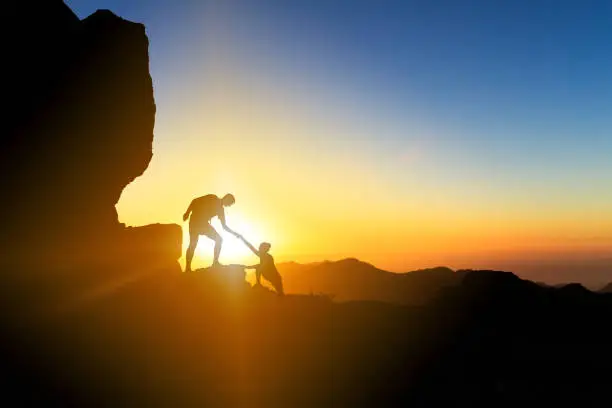 Teamwork couple helping hand trust help silhouette in mountains, sunset. Team of climbers man and woman hikers, help each other on top of mountain, climbing together, inspiring landscape on Gran Canaria