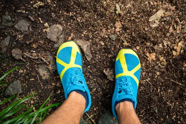 Trail runner looking down at sports shoe, running and training in nature. Man runner working out outdoors in nature.